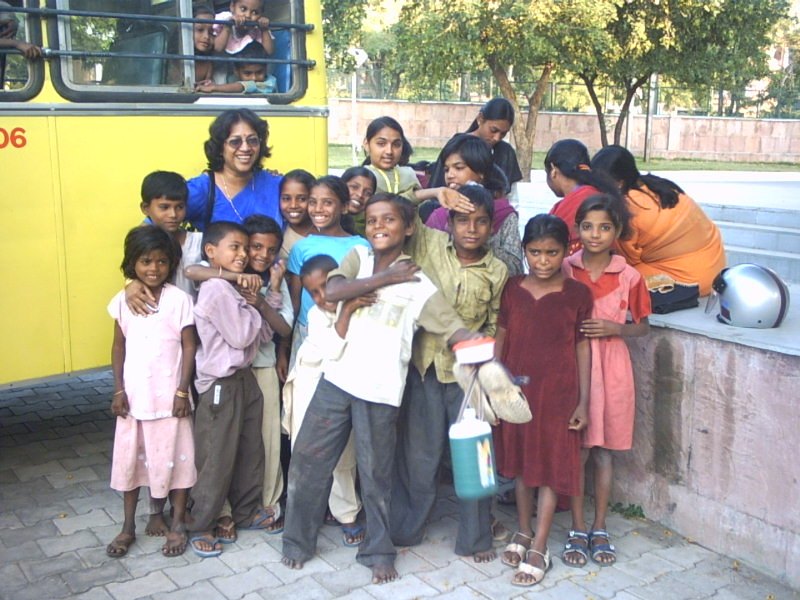 Children crowded around the door of the yellow school bus with a teacher, more children waving from the windows.
